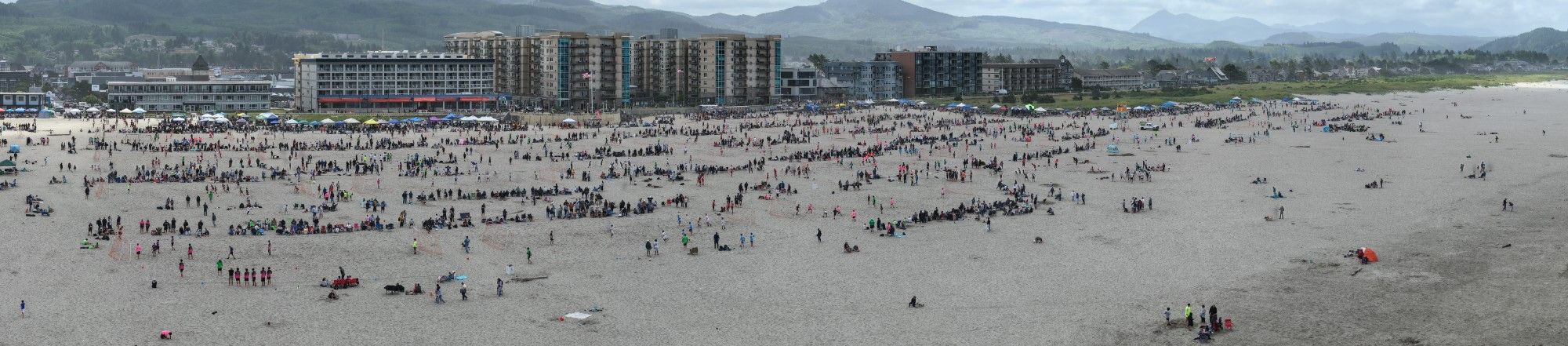 Aerial view of a packed Soccer In The Sand beach tournament, hundreds of players and spectators across the sand